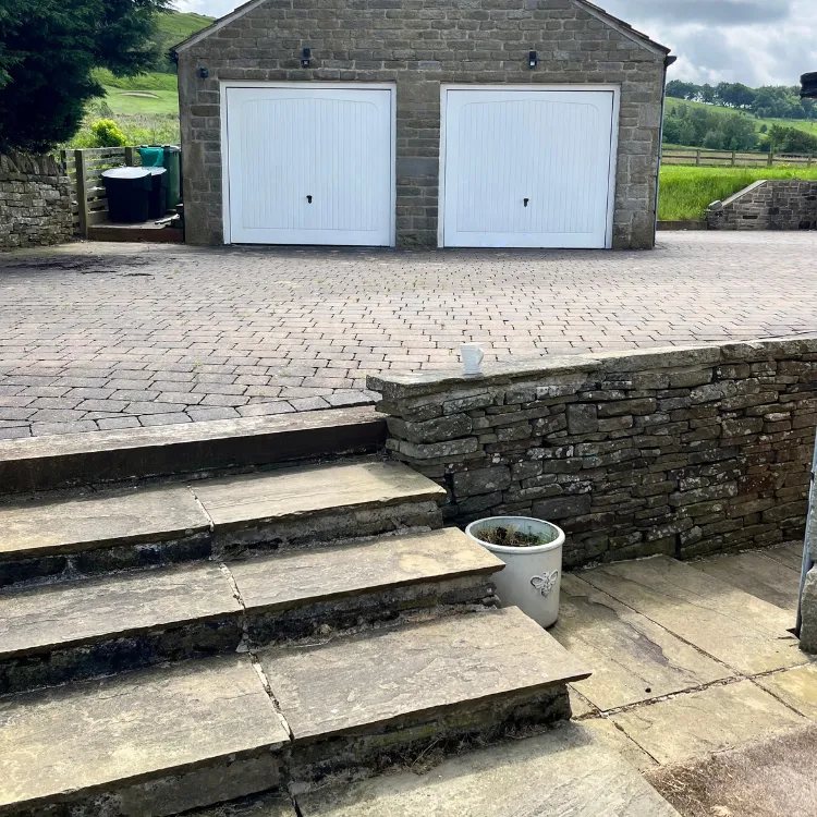 Block paved driveway and stone steps in front of a double garage before cleaning