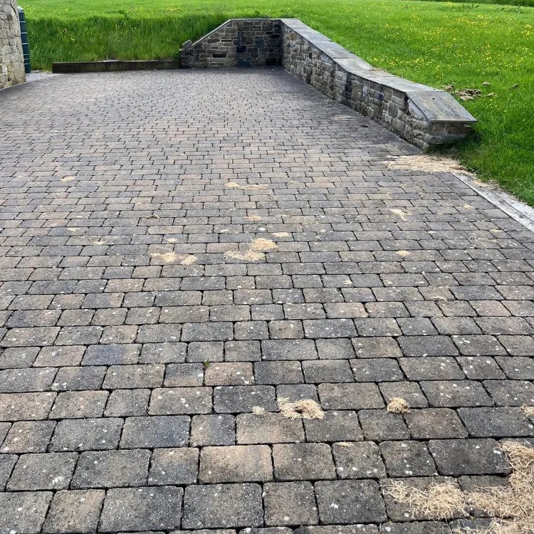 Block paving beside a dry stone wall before pressure washing, dark and weathered