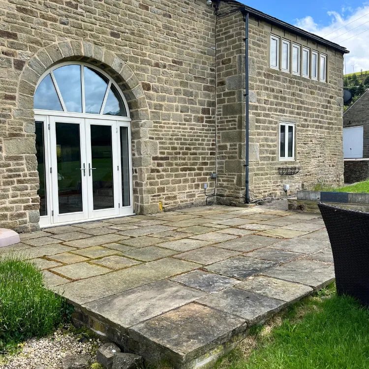 Stone patio in front of an arched doorway before pressure washing, grey and weathered