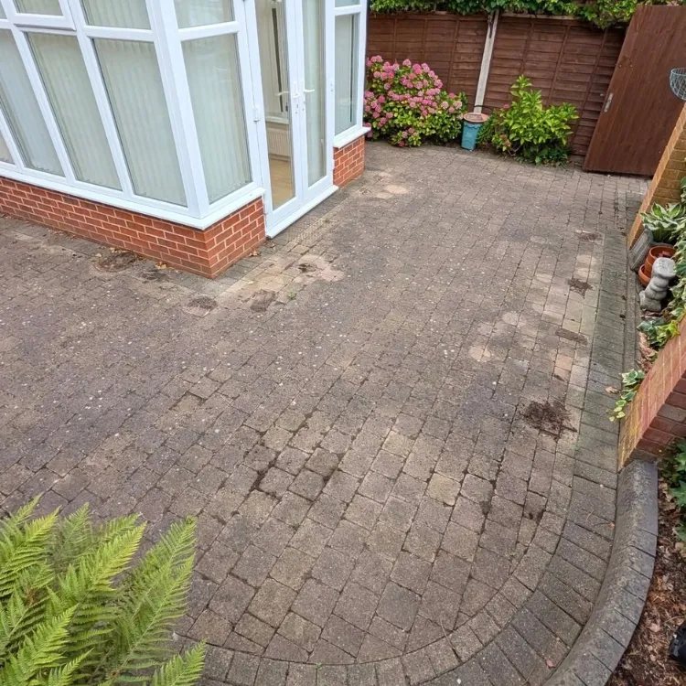 Block paved patio beside a conservatory before jet washing, dark and stained