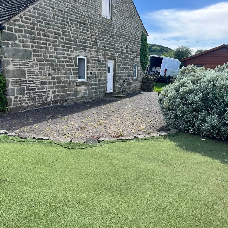 Block paving behind a stone house before pressure washing, dark and weedy