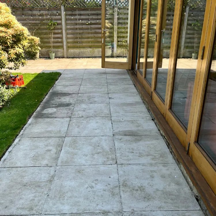 Tiled patio beside bifold doors before pressure washing, grey and marked