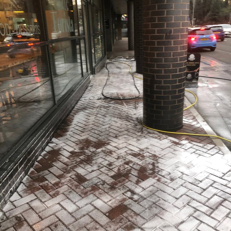 Cleaning treatment foaming on block paving outside a cafe, hose running to the van