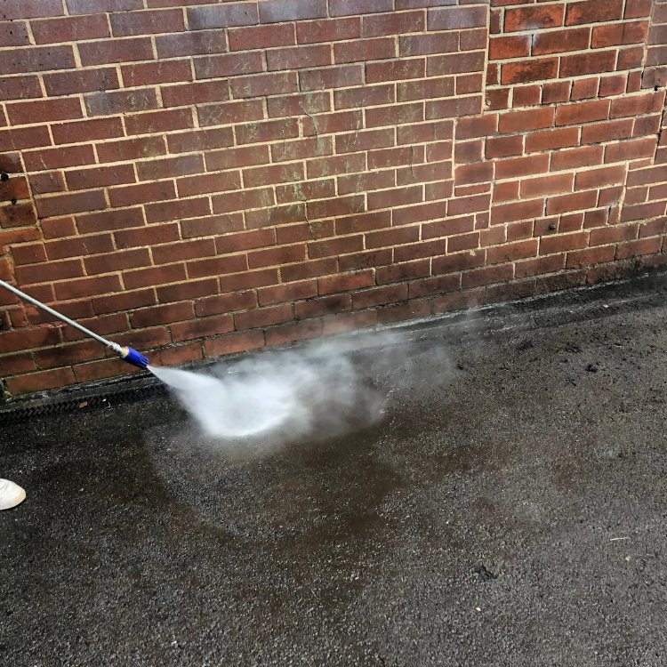 Pressure washing jet hitting the base of a brick wall