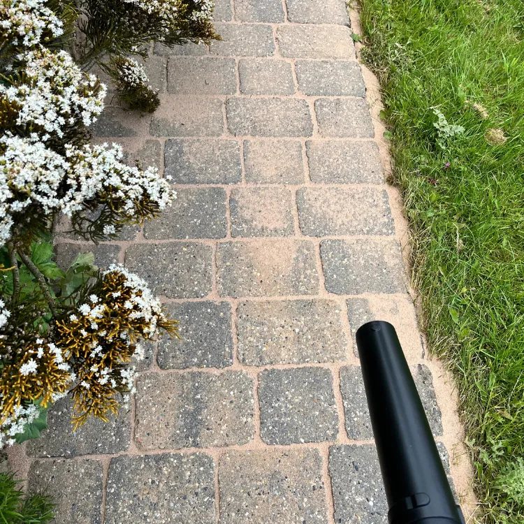 Leaf blower clearing loose sand from block paving