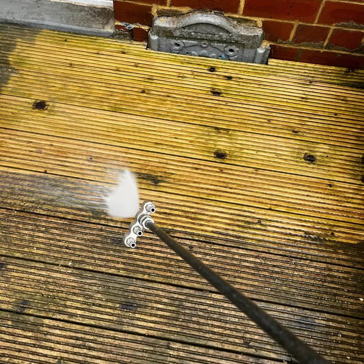 Wide angle nozzle cleaning timber decking, a clean strip showing against the green boards