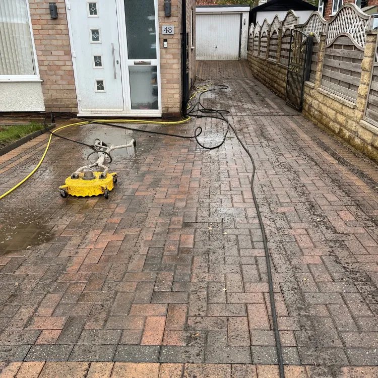 Rotary surface cleaner on a red block paved driveway, hoses running back to the van