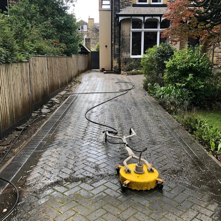 Rotary surface cleaner working along a wet herringbone block paved driveway