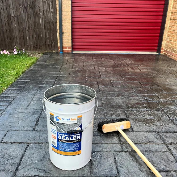 Tub of SmartSeal imprinted concrete sealer and a brush on a freshly sealed driveway