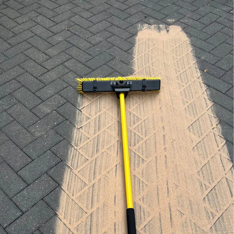 Broom sweeping kiln dried sand into the joints of charcoal block paving