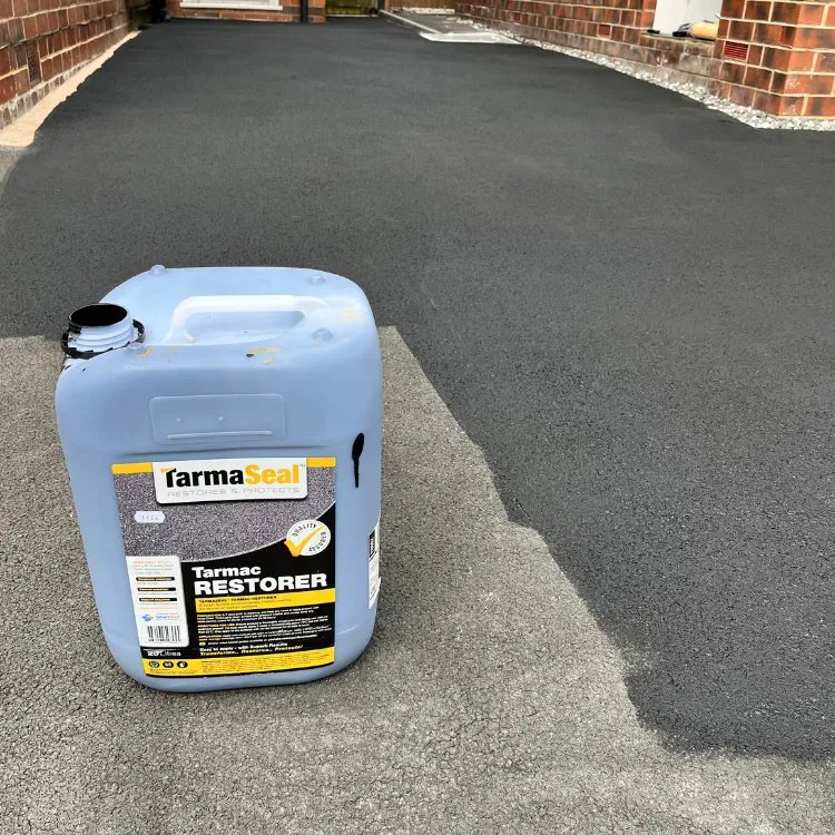 Drum of tarmac restorer standing on a part coated driveway