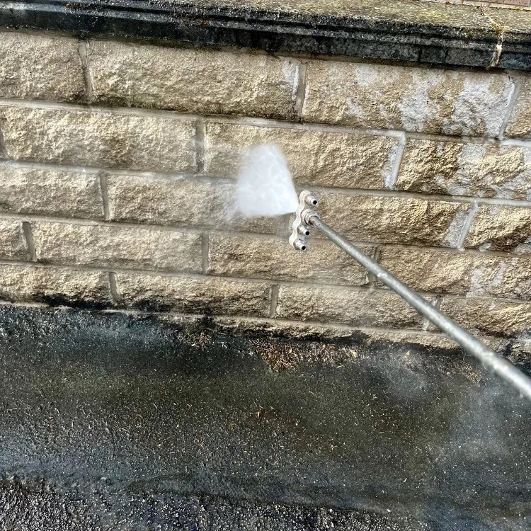 Pressure washing nozzle cleaning a stone garden wall, clean stone above the dirty band